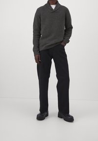 Mörkgrön stickad tröja med sjalkrage, kombinerat med svarta byxor och svarta grova stövlar. Slät yta och avslappnad passform.