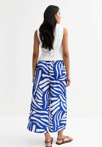 Top bianco senza maniche con un design aderente, abbinato a pantaloni blu a gamba larga con un motivo astratto bianco. Sandali marroni completano il look.