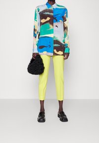 Färggad långärmad skjorta med abstrakta mönster i blått, gult och brunt, parat med ljusgula slim-fit byxor och svarta skor.