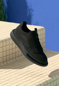 Baskets noires avec une tige en cuir lisse, bout arrondi et semelle épaisse. Caractérisées par un design à lacets et un logo discret sur le côté.