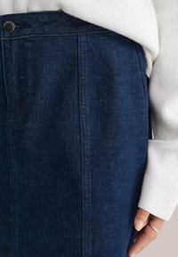 Sötétkék farmer szoknya egyenes szabással, felső gombos záródással és oldalsó zsebbel. Az anyag textúrált megjelenésű.