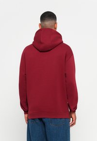 Burgundy hooded sweatshirt made of soft material, featuring a relaxed fit, ribbed hem, and dropped shoulders. No visible patterns or hardware.