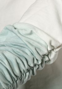 Manga de suéter ligera y fruncida que presenta un degradado de blanco a menta claro. Tela suave y texturizada con una superficie lisa.