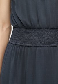 Gros plan d'une robe gris foncé avec une large ceinture froncée et une texture de tissu douce, mettant l'accent sur la taille et le bas du torse.