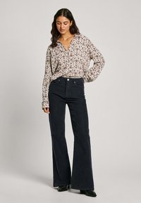 Blusa de manga larga con estampado floral en crema y colores oscuros; jeans negros de tiro alto y acampanados; botines negros. Fondo liso.
