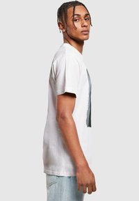 Hvit bomull t-skjorte med korte ermer, med grafisk design på forsiden. Passformen er avslappet, stylet med lyse denimjeans.
