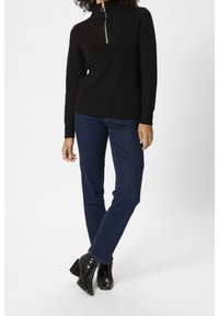 Schwarzer, gerippter Rollkragenpullover mit goldfarbenem Reißverschluss, kombiniert mit blauen Jeans mit geradem Bein und schwarzen ankle Boots mit Absatz.