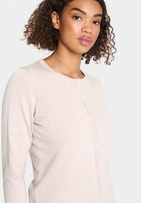 Cardigan beige en tissu tricot léger, avec un col rond, des manches longues et de petits boutons en perles pour les fermetures à l'avant.