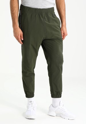 Grüne Jogginghose mit elastischem Bund, seitlichen Taschen und schwarzen Streifen. Das Material wirkt leicht und glatt.