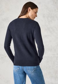 Un pull en tricot bleu marine avec un col rond et des poignets côtelés, associé à un jean en denim bleu clair avec des poches arrière.