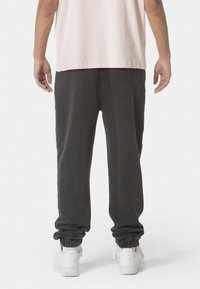 Dunkelgraue, zulaufende Jogginghosen mit elastischen Bündchen, aus weichem Material, kombiniert mit weißen Sneakers. Der Bund ist für einen hohen Tragekomfort zugeschnitten.