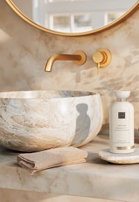 Bol en marbre avec un motif beige tourbillonnant, robinet et accessoires en or, bouteille de shampoing blanche, serviette beige douce. Ambiance de salle de bain minimaliste.