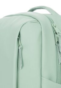 Light green backpack with a smooth texture, featuring a rounded shape and dual zipper hardware on the front.