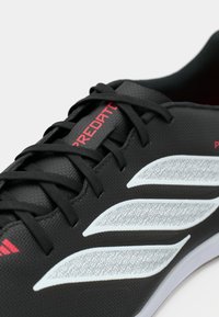 Μαύρο αθλητικό παπούτσι με υφή, κατασκευασμένο από συνθετικό υλικό, με αντίθετες λευκές ρίγες και γραφικό σχέδιο, καθώς και κόκκινο λογότυπο.