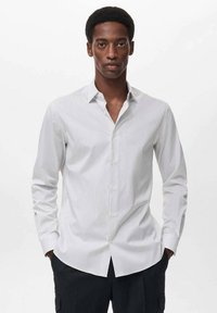 Camisa blanca de manga larga con rayas verticales en azul marino, cuello tipo button-down y diseño ajustado. Tejido suave con un brillo sutil.