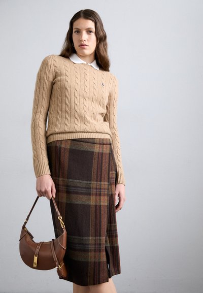 Beige cable-knit sweater with a white collar, paired with a brown plaid skirt featuring orange and green lines. Holding a brown leather handbag.