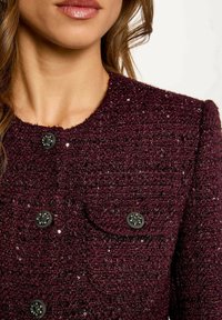 Giacca bordeaux con texture, caratterizzata da bottoni neri e paillettes, con scollatura tonda e tasche applicate sul petto.