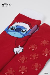 Chaussettes rouges comportant un personnage de dessin animé au visage bleu, avec un bord en fausse fourrure blanche et des motifs brillants de flocons de neige sur la semelle.