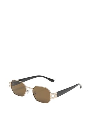 Lunettes de soleil octogonales teintées marron avec fines montures métalliques dorées et branches en plastique noir, inclinées sur fond blanc.