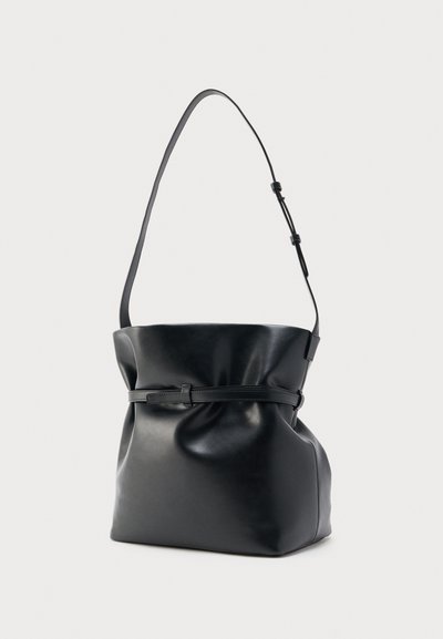Μαύρη δερμάτινη τσάντα ώμου με ρυθμιζόμενο λουράκι και λεπτή ζώνη στη γύρω από το πάνω μέρος στο κέντρο, μαλακός, χαλαρός σχήμα, σε ανοιχτό φόντο.
