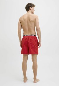 Červené plavky vyrobené z lehkého materiálu s elastickým pasem, které mají značení "JACK & JONES" a zadní kapsu na patku.