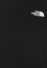 Svart t-shirt i bomull med en mjuk textur som har en vit logotyp av "The North Face" på den övre vänstra bröstområdet.