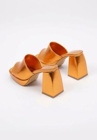 Las mule metálicas naranjas presentan una punta abierta cuadrada, un empeine curvado y tacones cuadrados gruesos. Textura suave con un acabado brillante.
