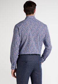 Herrskjorta med lång ärm i blommönster i blått, rött och vitt, med klassisk krage och knappmanchetter. Mörka, strukturerade byxor.