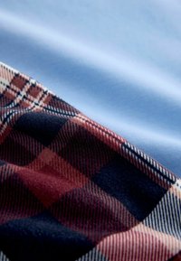 Bomuldsstof med blød, blå tekstur ved siden af et ternet mønster i rød, marineblå og creme, der viser bløde fibre og tydelige tern.