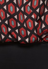 Gemustertem Stoff mit einem geometrischen Design in Rot, Blau, Weiß und schwarzen Formen. Glatte Textur, drapiert mit einer sichtbaren Naht.