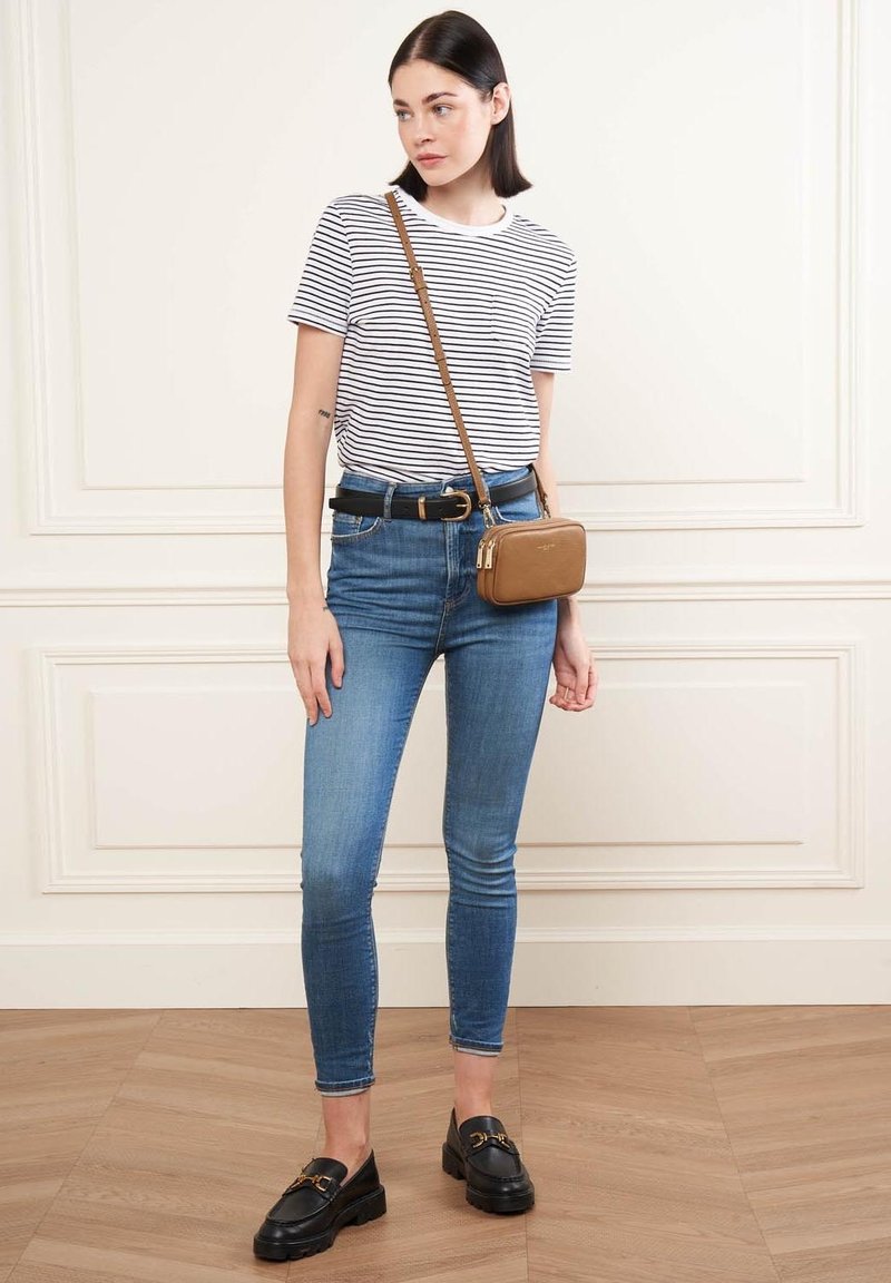 T-shirt a righe, jeans skinny blu, mocassini neri e una piccola borsa a tracolla marrone. Presenta un design aderente e uno stile informale.