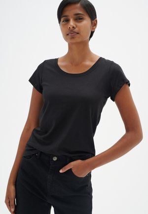 Svart kortärmad t-shirt med rund halsringning, gjord av mjukt bomullstyg. Slimmad design med uppvikta ärm, ihop med mörka jeans.