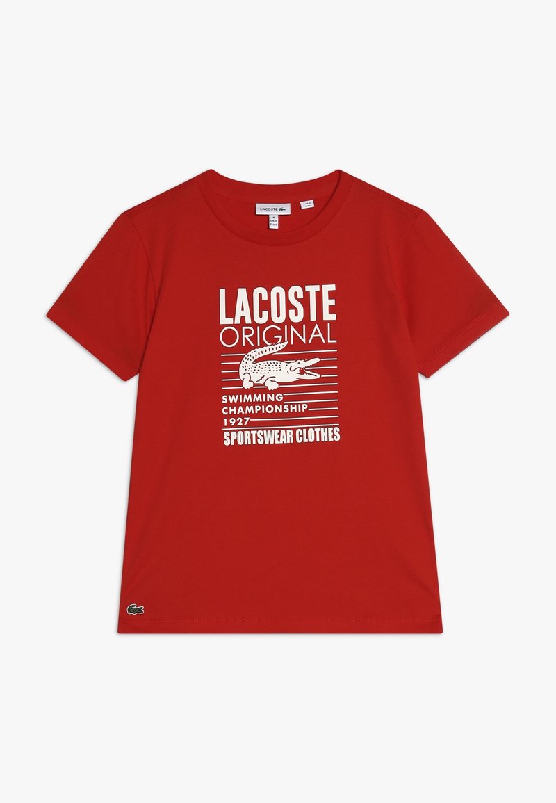 T-shirt rossa in cotone con un design grafico bianco, che include testo e un logo di coccodrillo, con scollo a girocollo e maniche corte.