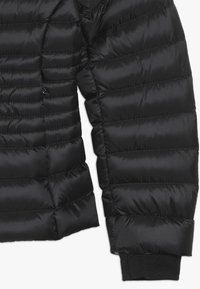 Schwarze Steppjackenärmel mit abgestepptem Textur, versehen mit Nählinien und einem gerippten Strickbündchen für Isolation und Passform.