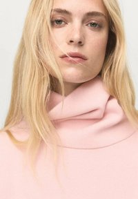 Maglione a collo alto rosa chiaro realizzato in tessuto morbido, con un design a collo piegato e una texture liscia. Vista ravvicinata dell'indumento.