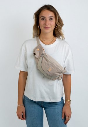 Beige crossbody bag made of fabric, featuring adjustable strap, zippered compartments, and a small logo patch. Smooth texture and minimalist design.