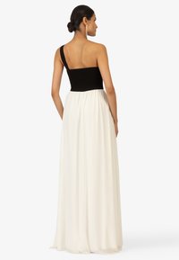 Schwarzes Kleid mit gerafftem Oberteil und einem Träger, fließendem weißen Rock, glatter Textur und knöchellangem Design. Die Rückansicht zeigt das Trägerdetail.