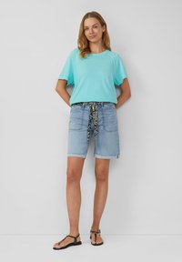 Lichtblauw t-shirt met korte mouwen, casual denim shorts met een zwart-witte gesp met patroon, en platte zwarte sandalen met een eenvoudig ontwerp.
