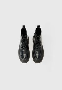 Bottines en cuir noir avec une semelle épaisse, ornées de lacets, d'une couture à l'avant et de passepoils sur chaque talon. Texture lisse et design moderne.