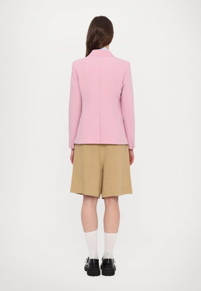 Pink tailored jacket with a notched collar, single back vent. Paired with beige shorts, white socks, and black shoes.