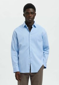 Jasnoniebieska koszula z długim rękawem i kołnierzykiem na guziki, z delikatnym wzorem w paski i białymi guzikami, w połączeniu z szarymi spodniami.