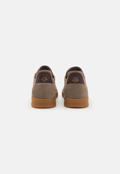 Brune ruskindssko med en lys tan gummisål. Bagsiden har et mørkerødt accent og et præget dekorativt logo. Rundet formdesign.