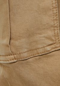 Tan denim med en slät textur, som har detaljerad sömnad och en framträdande fick söm. Tyget har en subtil, hållbar väv.