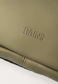 Olivgrünes Rains-Produkt mit mattem Finish, das geprägt ist und kontrastierende Nähte entlang der Kanten aufweist.