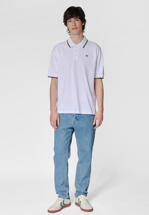 Hvid polo skjorte med sorte detaljer, afslappet pasform, båret med lyseblå jeans og hvide sneakers med grønne striber.