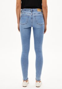 Jeans de mezclilla ajustados de color azul claro con una cintura alta, que cuentan con dos bolsillos traseros y una etiqueta de cuero marrón en la cintura. Textura de mezclilla suave.