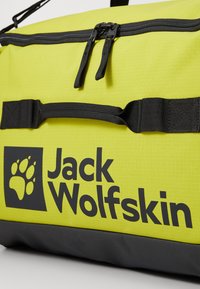 Felgekleurde gele duffelbag met zwarte accenten, voorzien van een dubbele rits, draagriemen en het Jack Wolfskin-logo aan de zijkant.