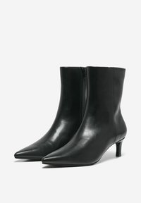 Bottes de cheville en cuir noir avec un bout pointu, un talon de hauteur moyenne et une fermeture à glissière sur le côté. Texture lisse avec un design épuré et minimaliste.