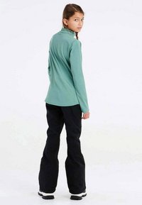 Groene top met lange mouwen in combinatie met zwarte broek. De top heeft een hoge kraag en de broek heeft een losse pasvorm met een gladde textuur.