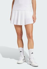 Hvit plisserte tennisrulle med hvite sokker og sneakers, med grå aksenter og strukturert stoff. Rent, atletisk design.